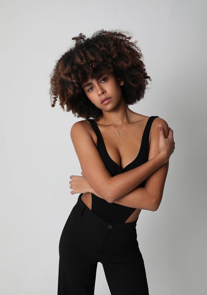 Model posing with curly hair in stylish outfit.