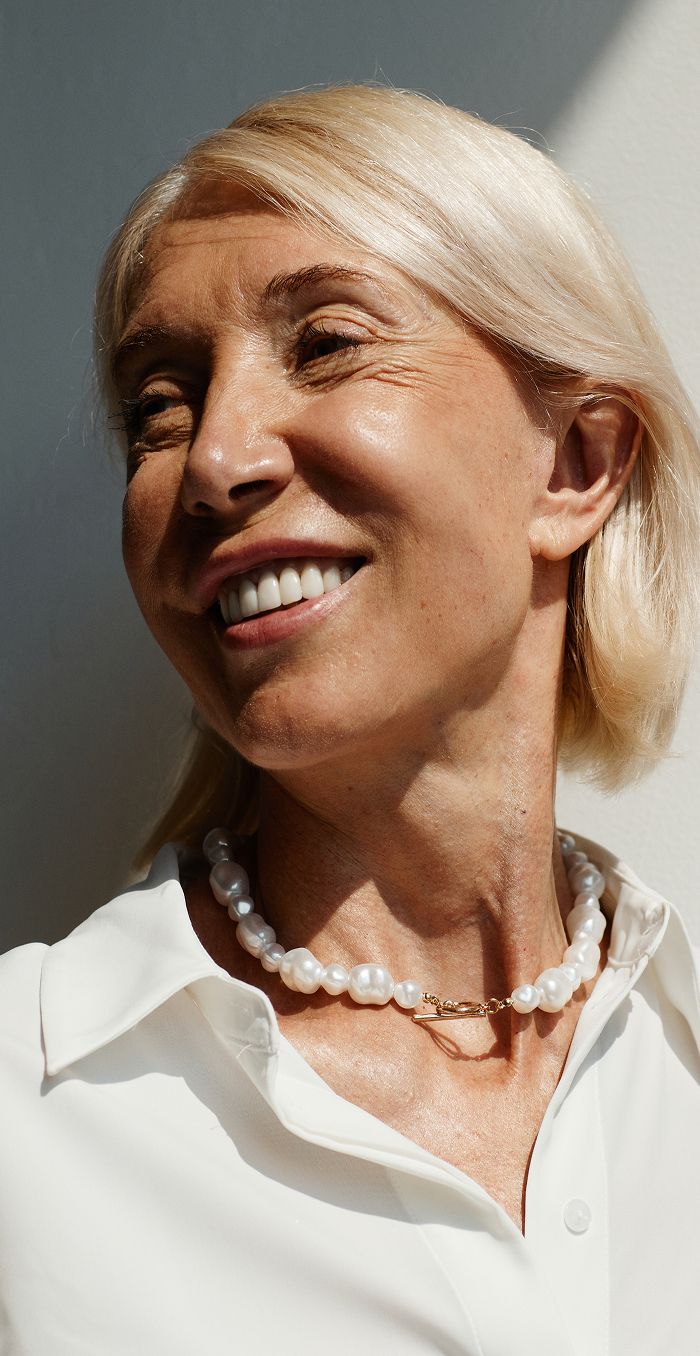 Smiling woman with pearl necklace and blonde hair.