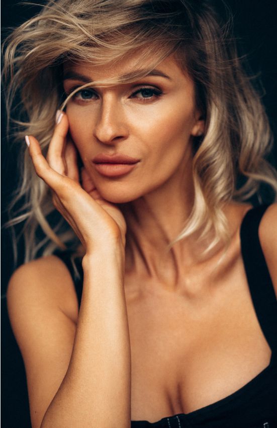 Woman with wavy hair posing thoughtfully against dark background.